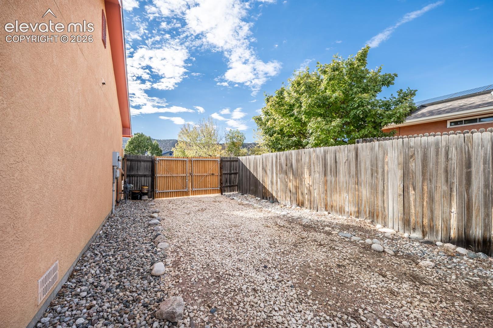 Side yard featuring stucco siding, gravel ground cover, and a wood privacy fence with a double-swing gate