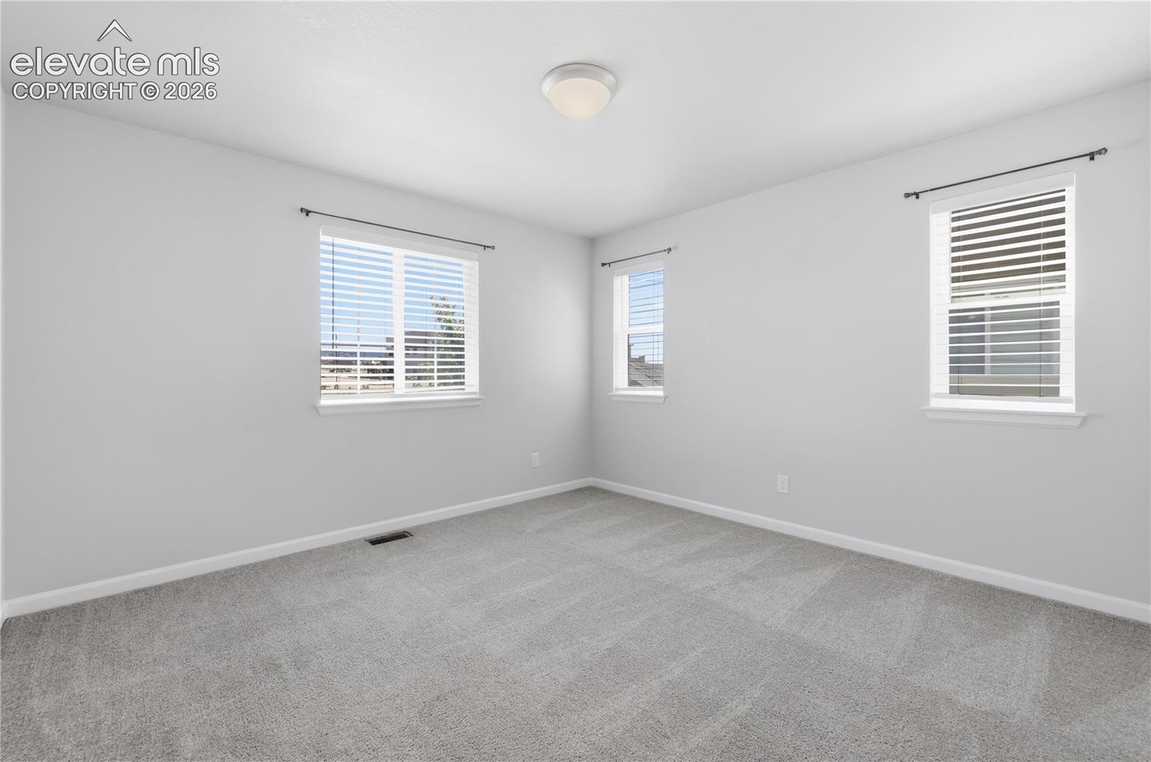 Neutral tone wall paint, light gray carpet flooring, multiple windows with blinds, white trim, and a flush mount ceiling light fixture