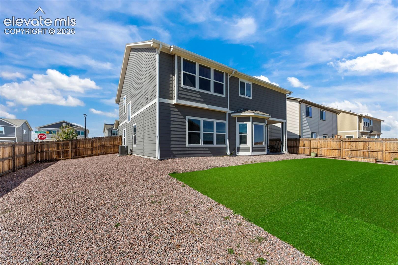 Two-story exterior with gray siding, white trim, and a fenced backyard featuring artificial turf and gravel