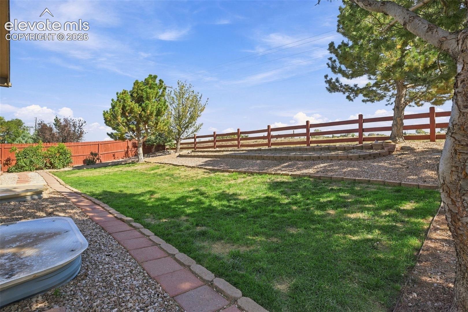Expansive outdoor space featuring a manicured lawn, established trees, and a wooden fence