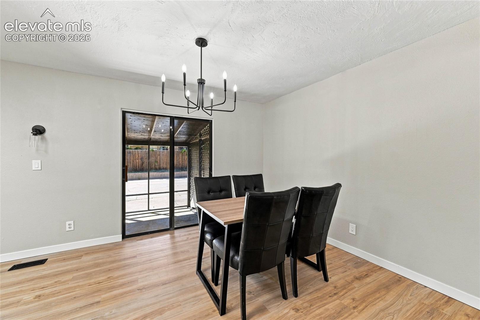 Wood-finish flooring, light gray walls, black framed sliding glass door, modern black chandelier, and white trim