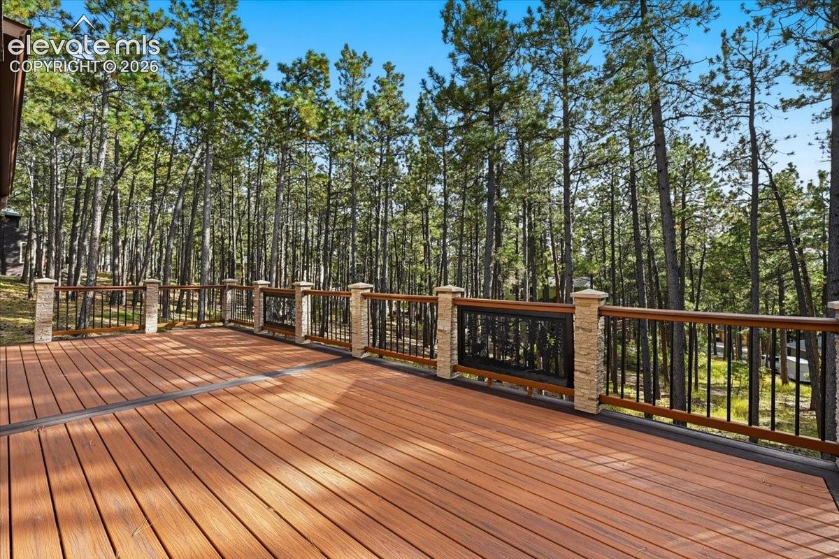 Expansive composite deck with wood-finish planks, stone-clad railing posts, and a metal and wood railing system, surrounded by mature trees