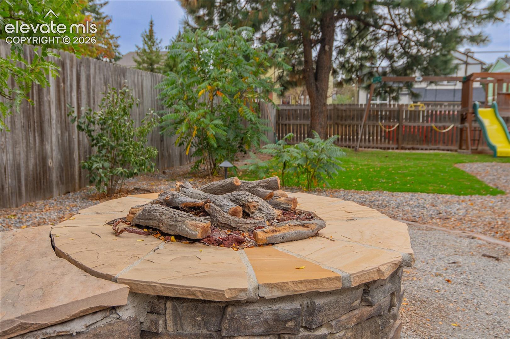 Stone fire pit with flagstone capping, gravel surround, and wood privacy fencing