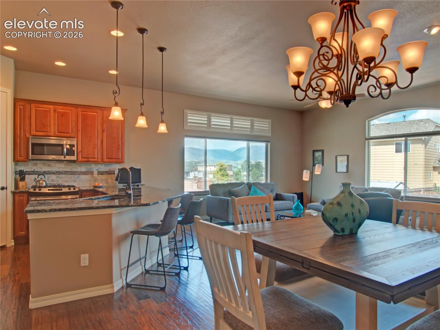Open-concept living space featuring wood-finish flooring, a kitchen with rich wood cabinetry and stainless steel appliances, and a dining area with a wrought iron chandelier