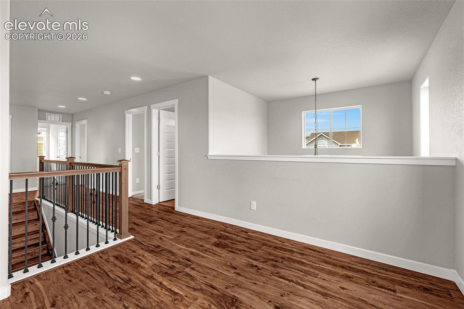 Upper landing featuring wood-finish flooring, white walls, and a wrought iron and wood balustrade