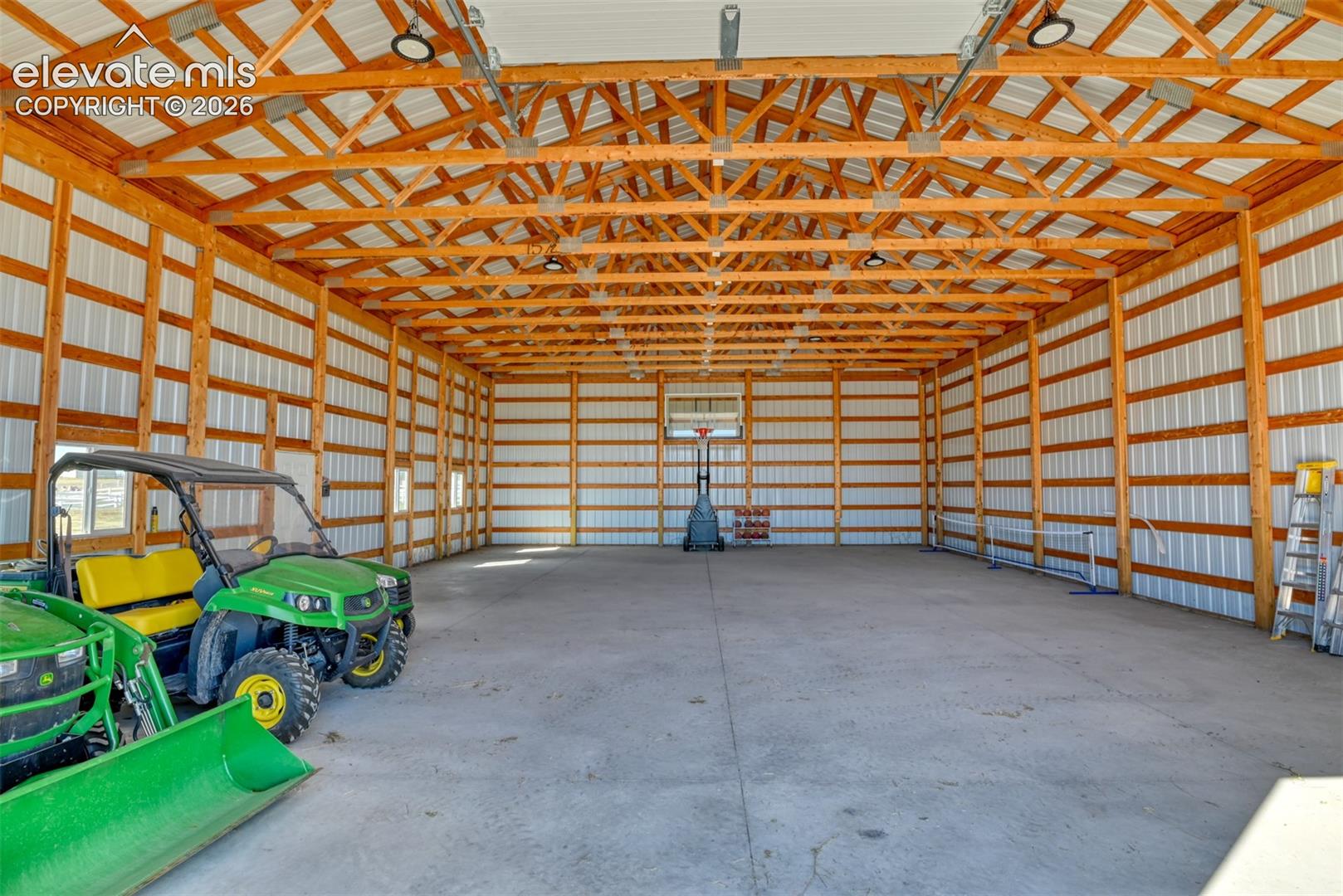 Expansive barn interior featuring exposed wood beam construction, corrugated metal walls, concrete flooring, and overhead lighting fixtures