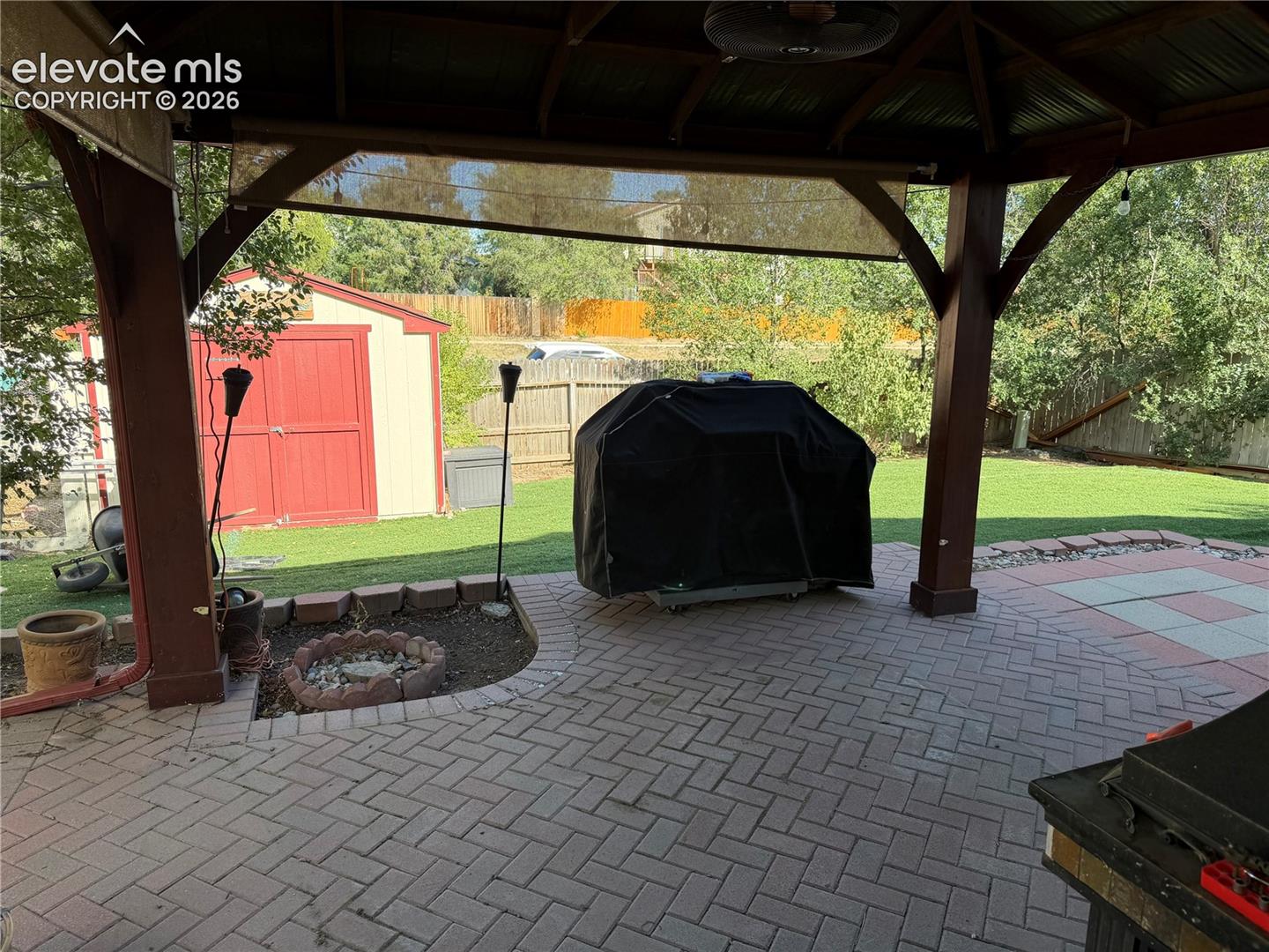 Covered patio with a multi-tone paver floor, a built-in fire pit, and a detached storage shed