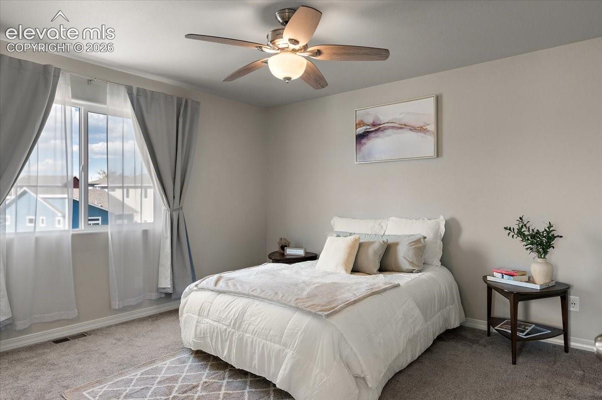 Bright secondary bedroom featuring a ceiling fan with integrated lighting, expansive windows with thermal-lined curtains, neutral wall finishes, and carpeted flooring