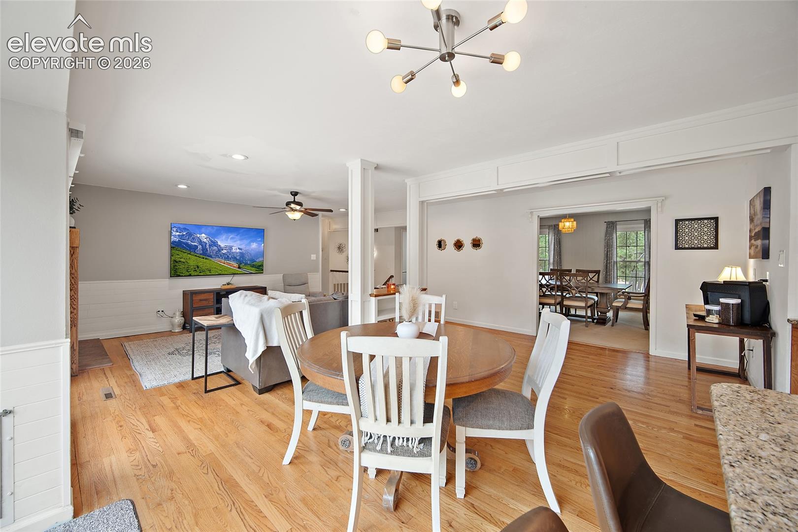 Open-concept interior featuring wood-finish flooring, white wainscoting, mid-century modern sputnik-style ceiling lighting, and structural support columns