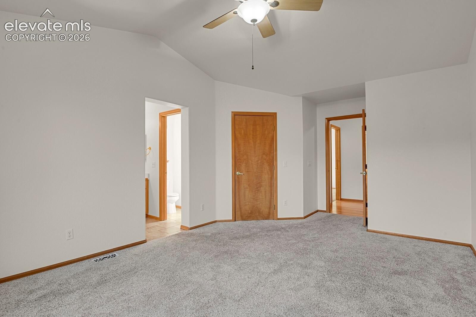 Light gray carpeting with wood-finish trim, vaulted ceiling, and ceiling fan