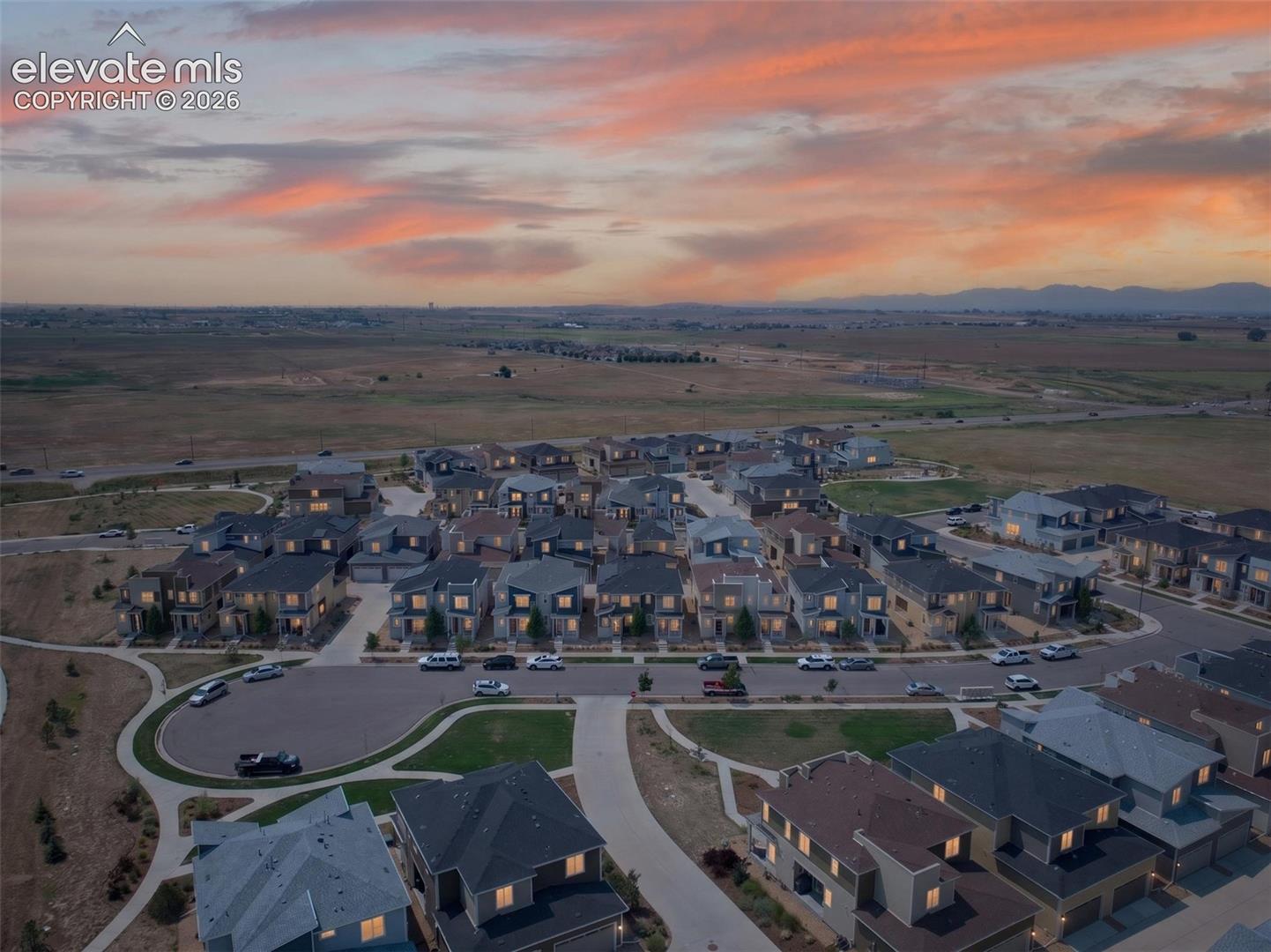 Aerial perspective of a planned community featuring multi-story residential structures, paved streets, concrete sidewalks, and an expansive horizon with a mountain range backdrop