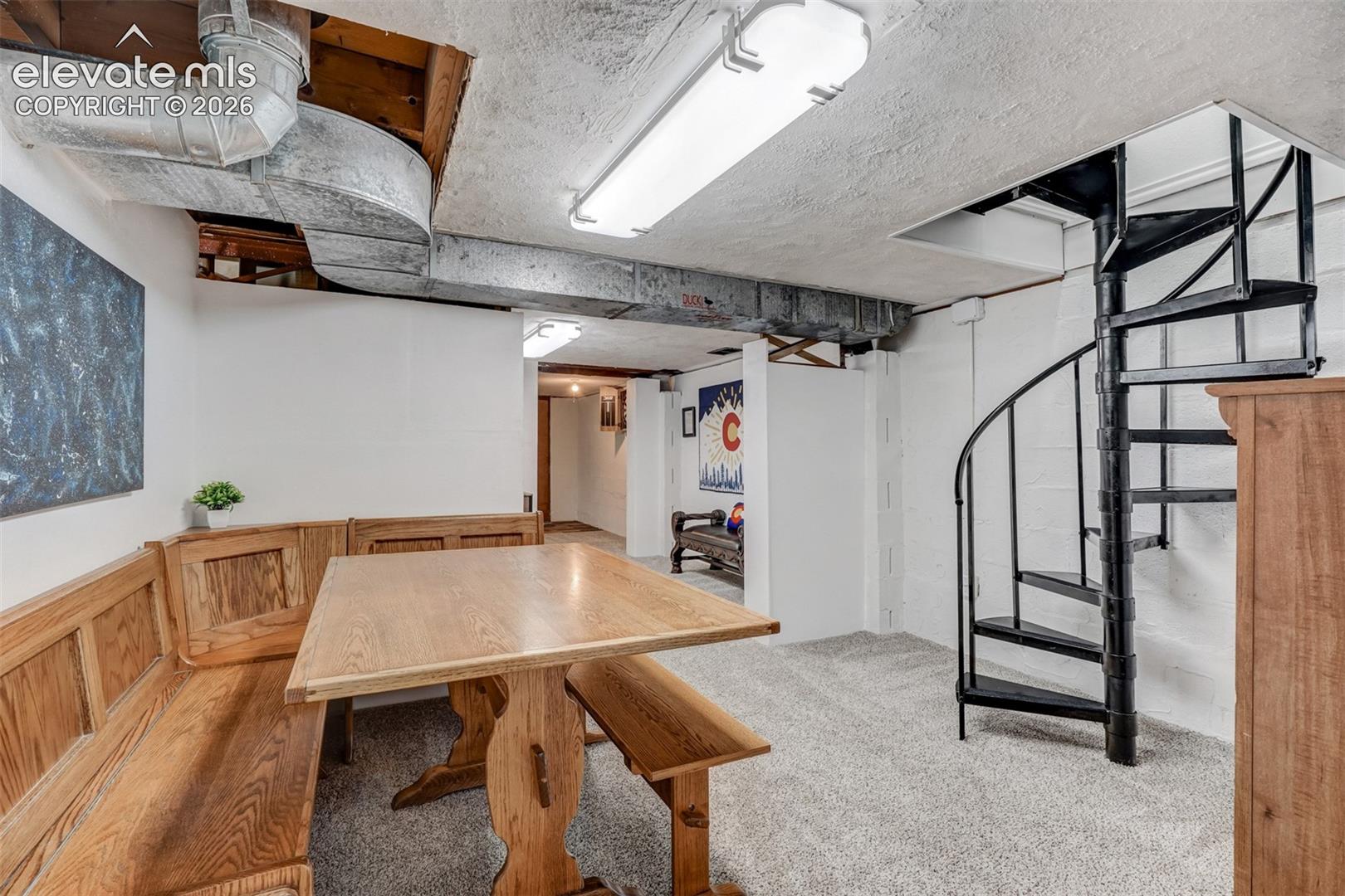 Carpeted interior space featuring a black spiral staircase, exposed ceiling ductwork, and built-in wood bench seating