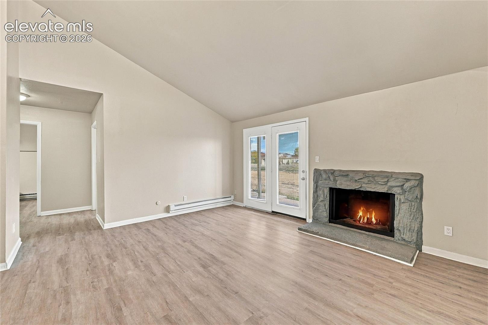 Vaulted ceilings, wood-finish flooring, and a fireplace featuring a stone-style hearth and surround, punctuated by glass-paned double doors