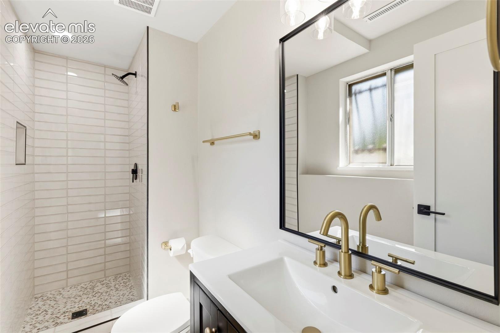 Bathroom featuring a frameless glass shower enclosure with horizontal tile, a built-in shower niche, and a pebble shower floor