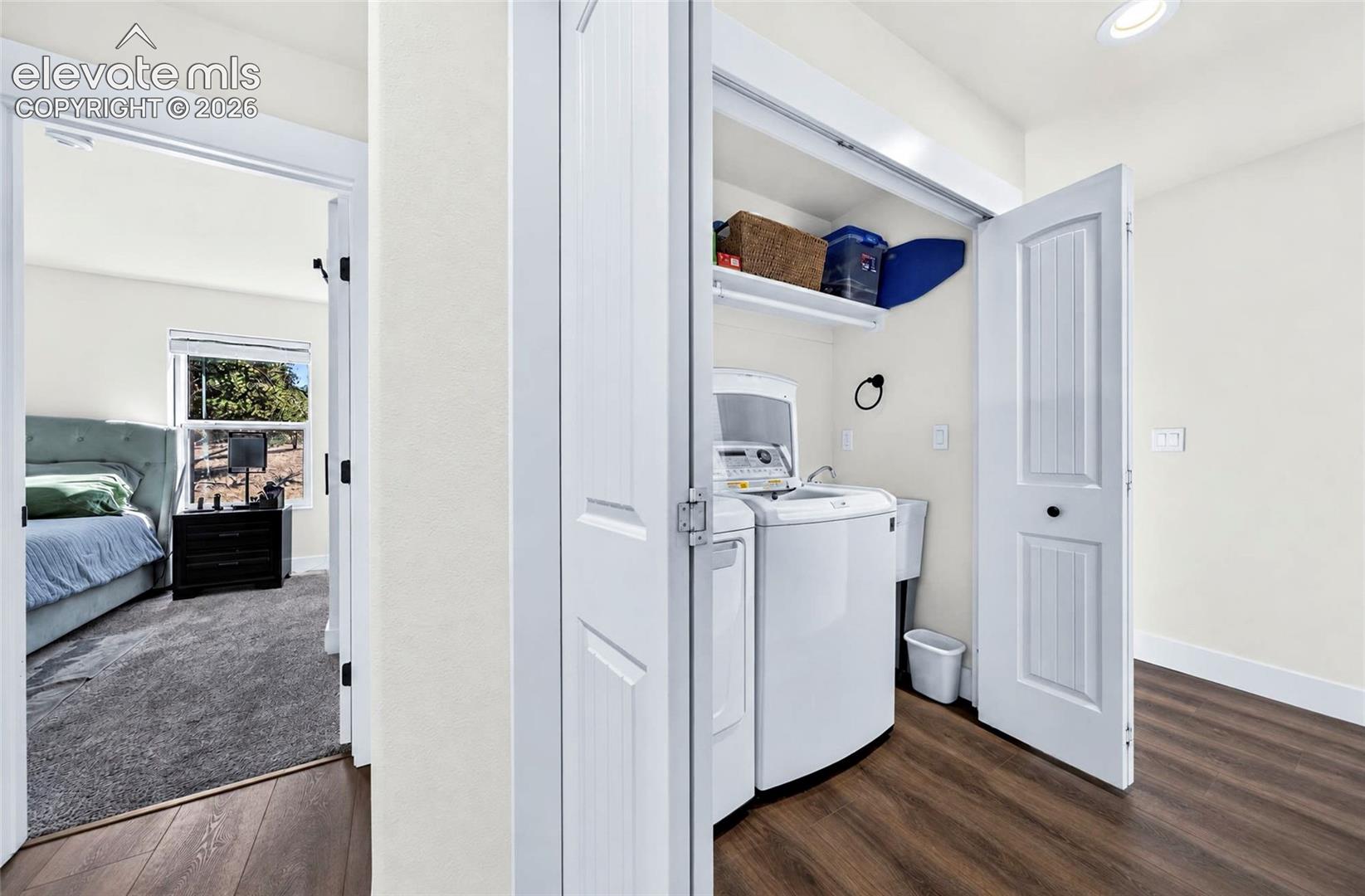 Laundry closet featuring folding bi-fold doors, overhead shelving, and a utility sink, set against wood-finish flooring