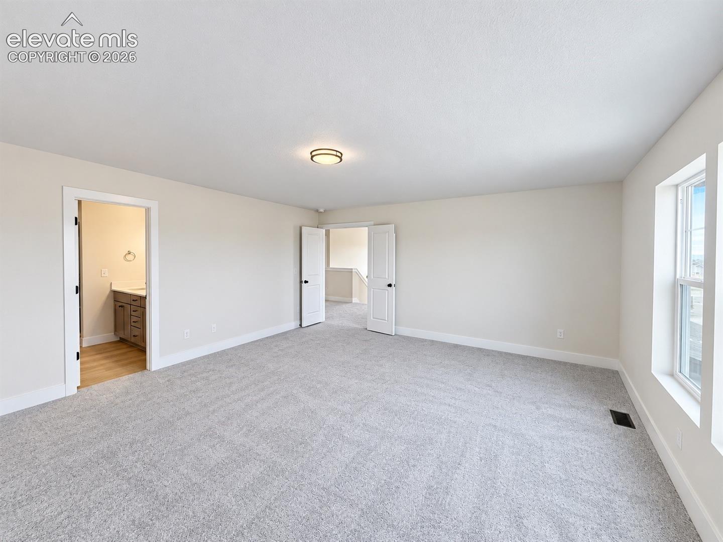 Spacious room featuring neutral carpeting, a dual-door entrance, an overhead flush-mount light fixture, and large windows