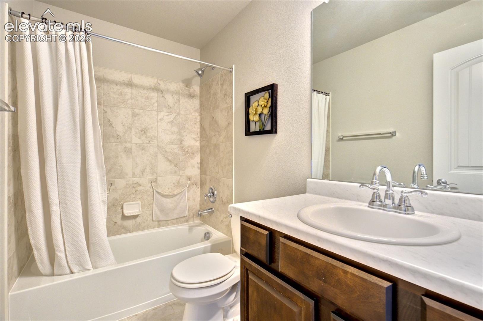 Bathroom featuring a vanity with a white countertop and oval under-mount sink, dark wood-finish cabinetry, a full-width mirror, and a tub-shower combination with tiled surround