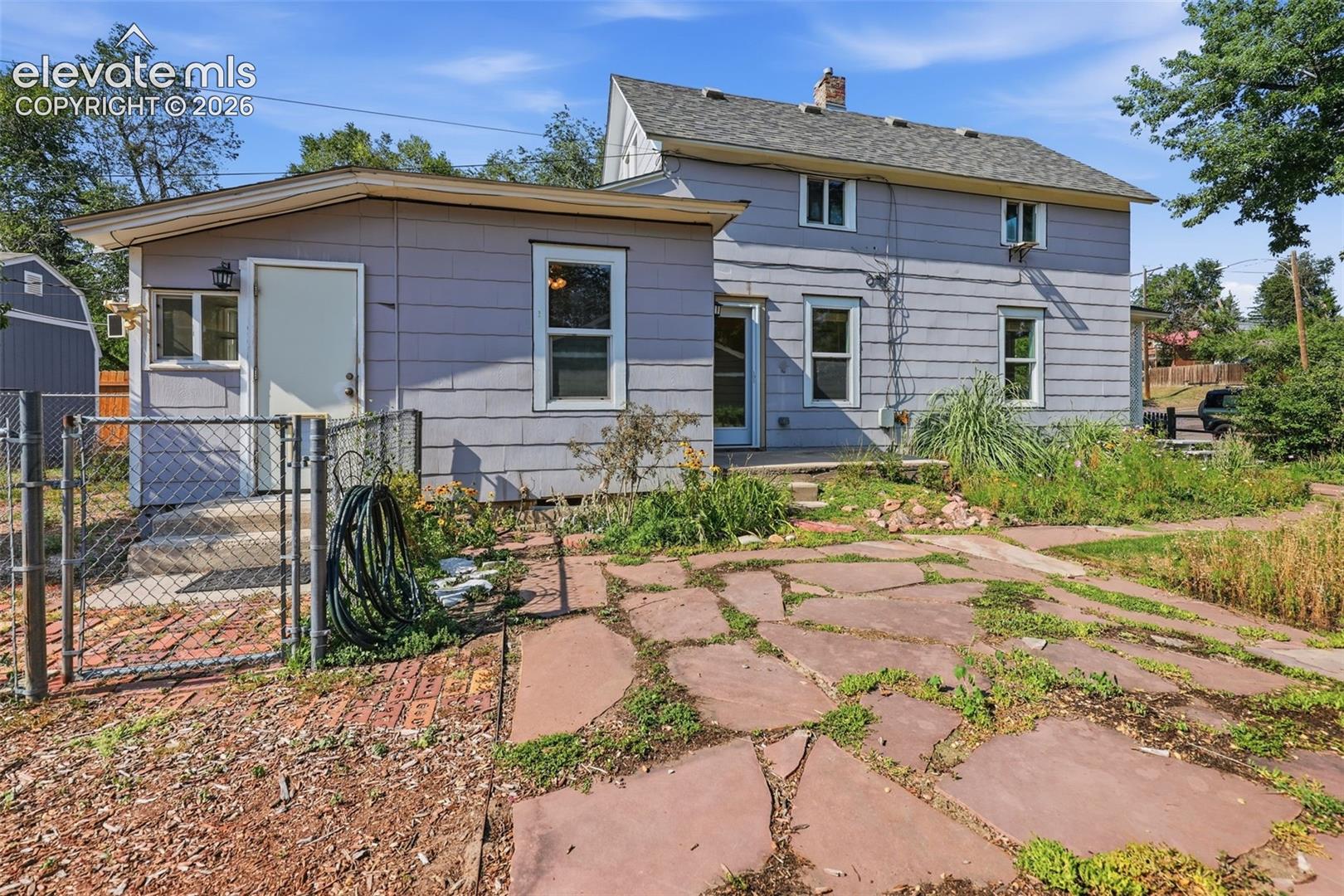 Side of structure exterior featuring a flowerbed, horizontal siding, white trim windows, two side door yard access, and flagstone paving.