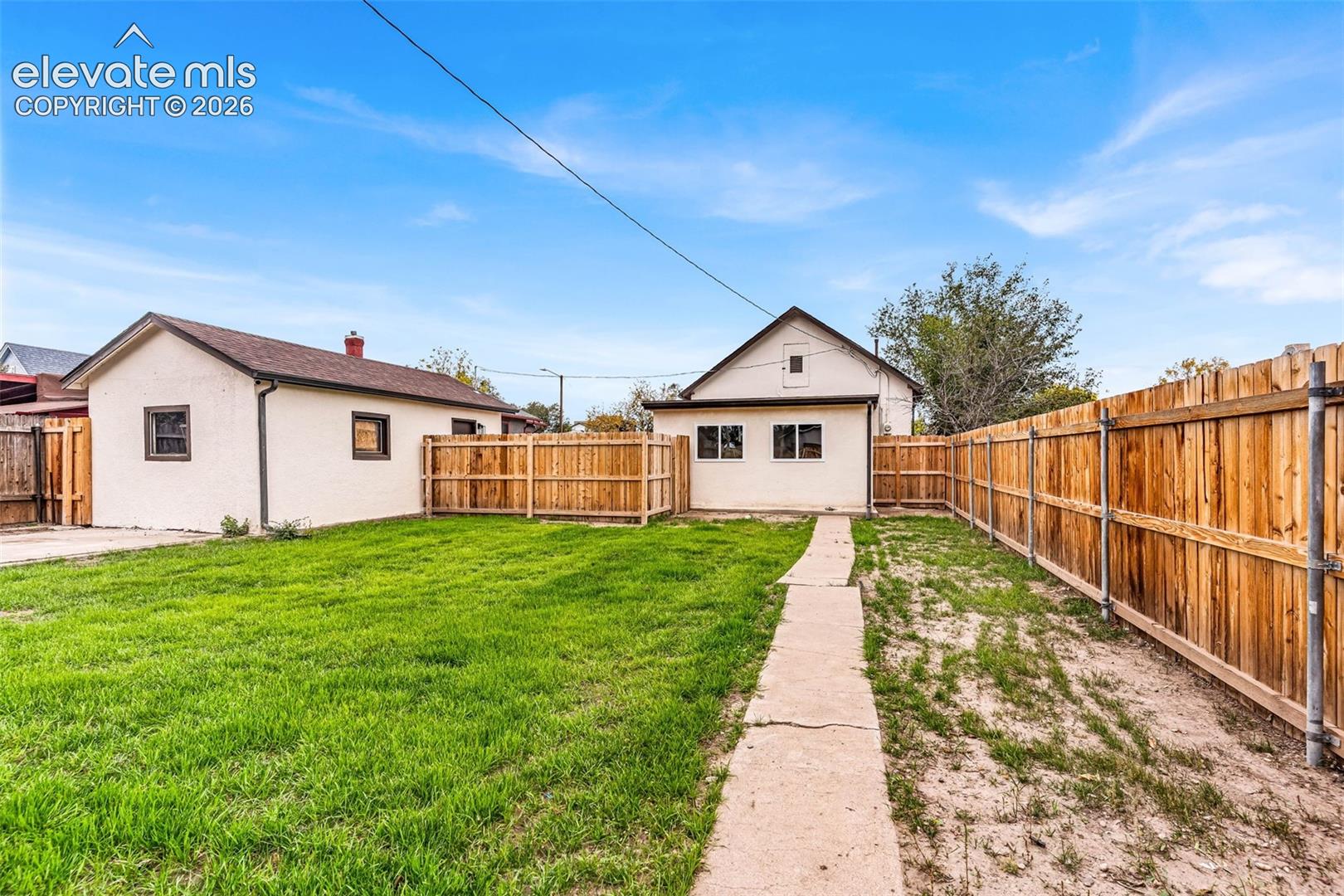 Fenced backyard featuring a grass lawn, concrete walkway, and detached structure