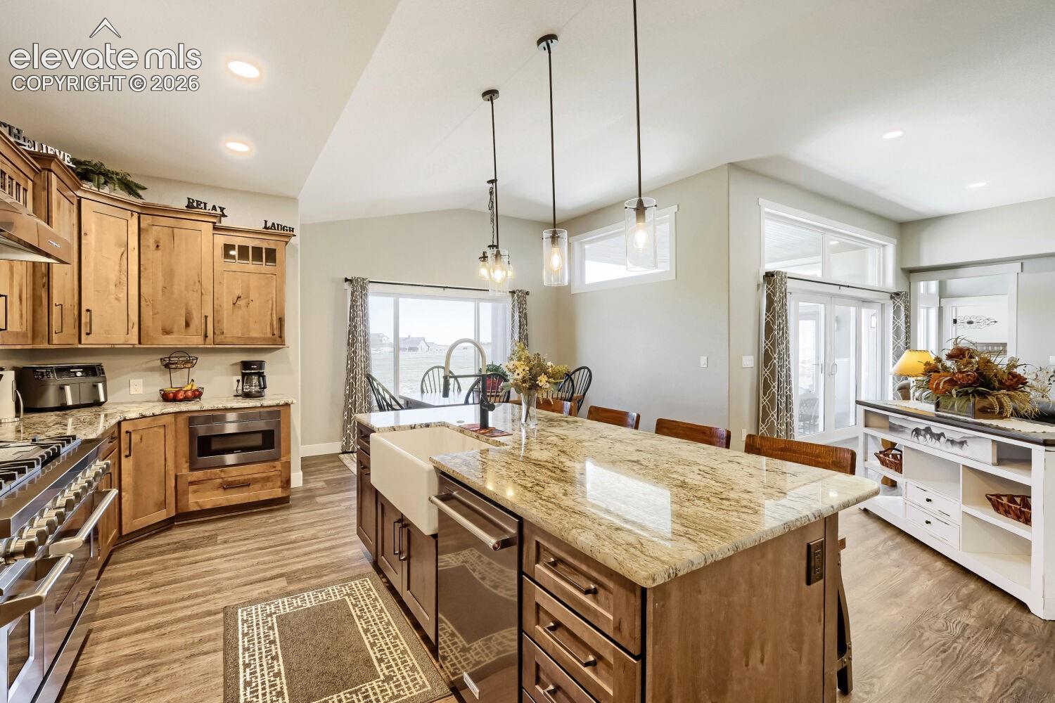 Kitchen featuring wood-finish flooring, natural wood cabinetry, light-toned granite countertops, and stainless steel appliances