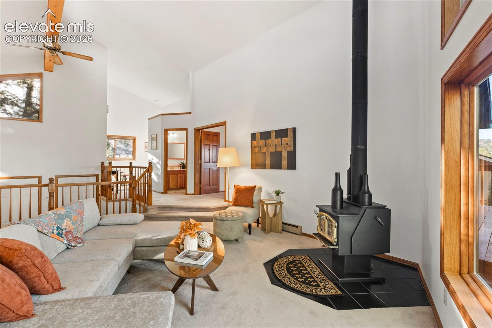 Vaulted ceilings, free-standing wood-burning stove on a tile hearth, wood-cased windows, and natural wood-finish railings