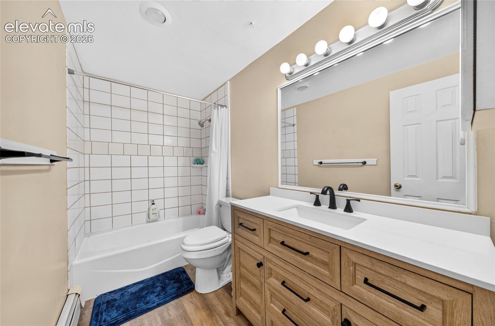 Wood-finish vanity with a rectangular sink, white countertop, matte black faucet, and large wall-mounted mirror featuring integrated lighting