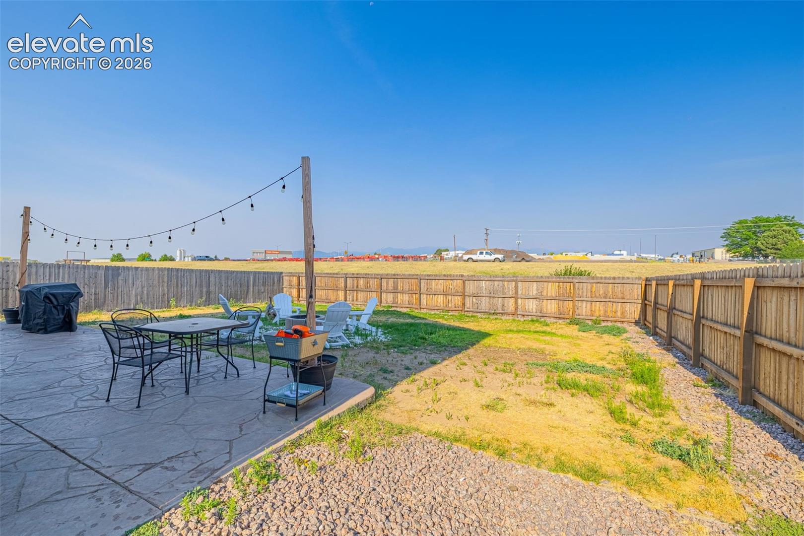 Expansive backyard featuring a concrete patio with string lighting, a gravel border, and a wooden privacy fence