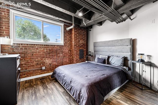 Bedroom featuring brick wall and wood finished floors