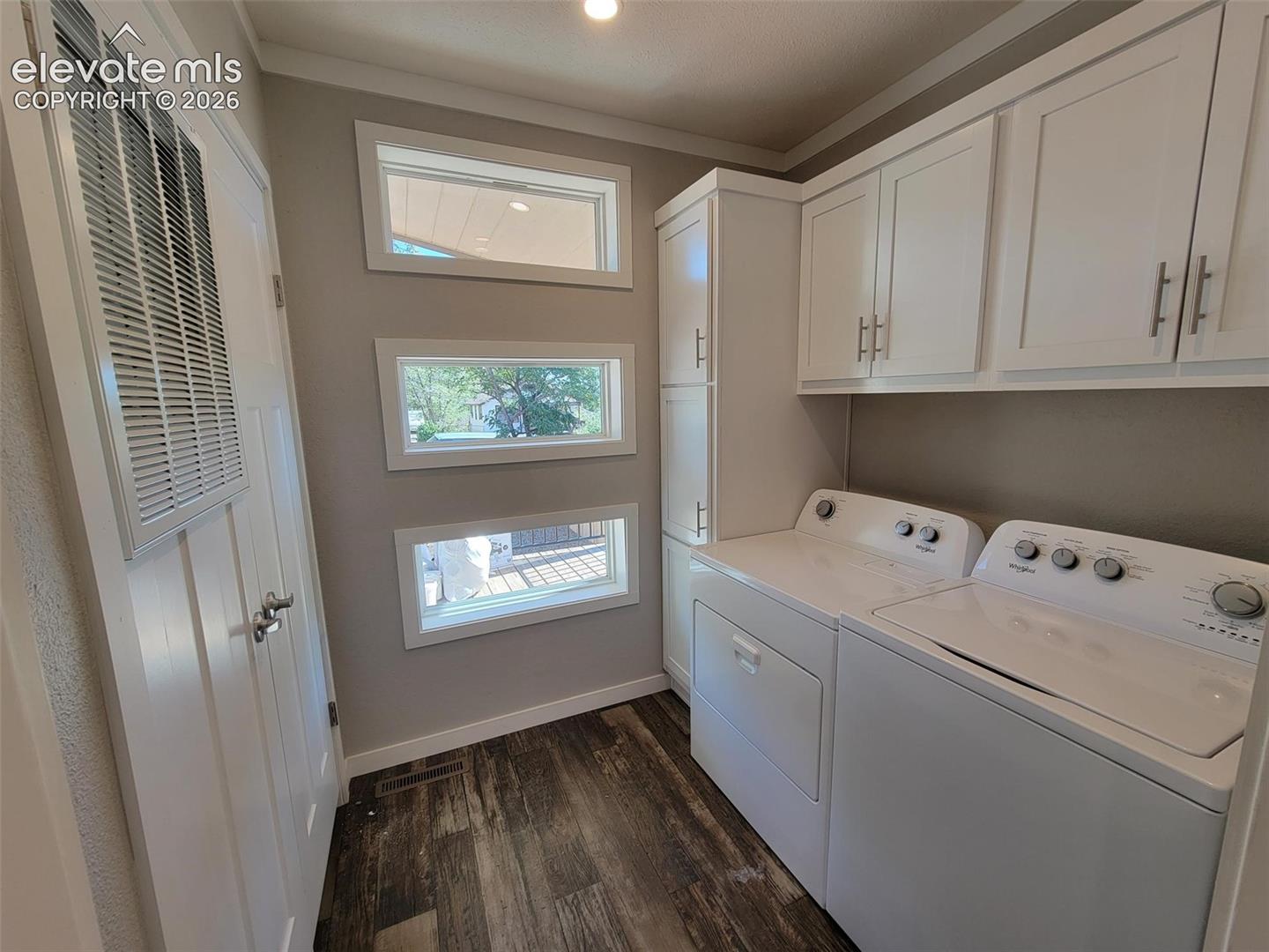 Laundry area featuring white shaker-style wall cabinets and full-height storage cabinetry, stacked horizontal windows, and wood-finish flooring