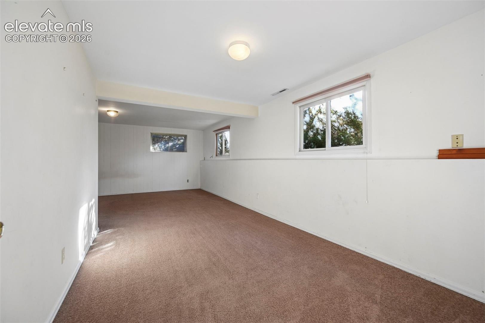 Spacious room with carpeted flooring, multiple windows, and overhead lighting