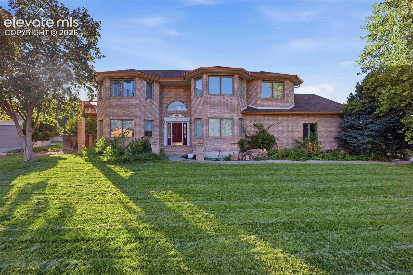 Brick exterior with multiple bay windows, an arched entry, and a large front lawn
