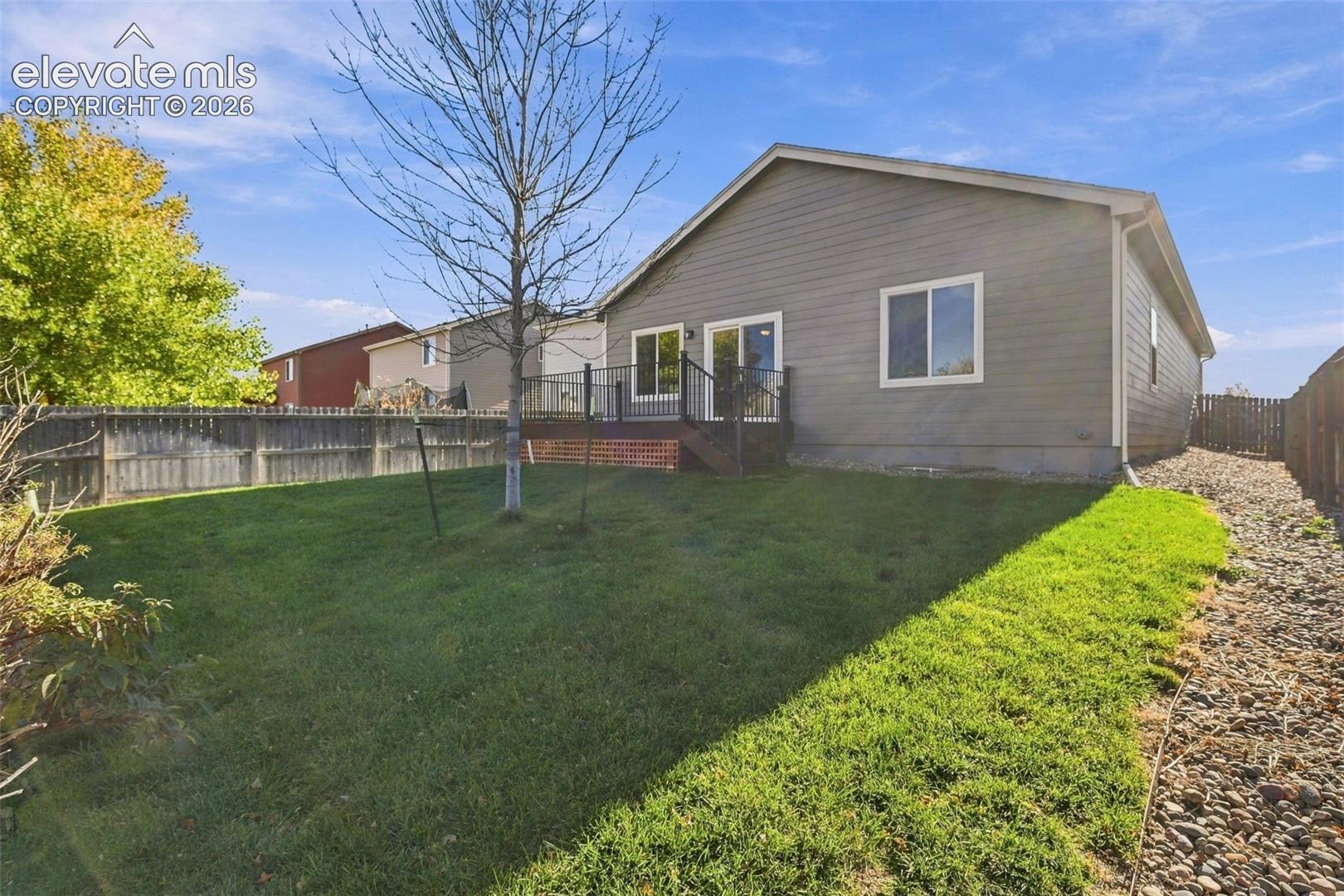 Rear exterior featuring horizontal lap siding, a raised deck with metal railings, a fenced perimeter, and a rock-mulched side border