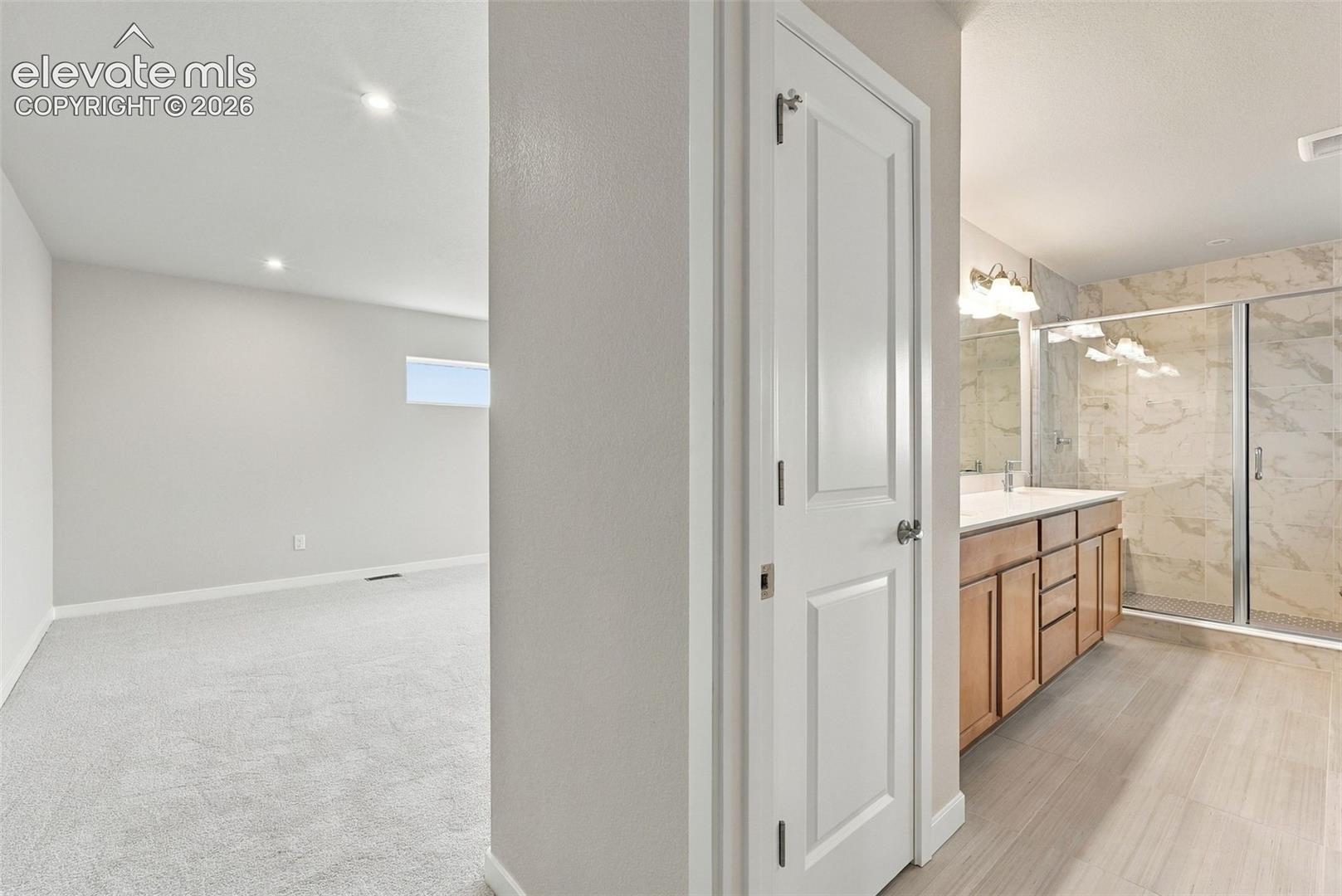 Bathroom featuring a wood-finish vanity with a light countertop, a walk-in shower with tile surround, and tile-finish flooring