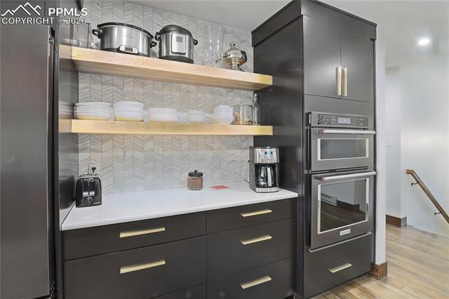 Kitchen featuring open shelves, dark cabinetry, stainless steel appliances, light wood-style floors, and decorative backsplash