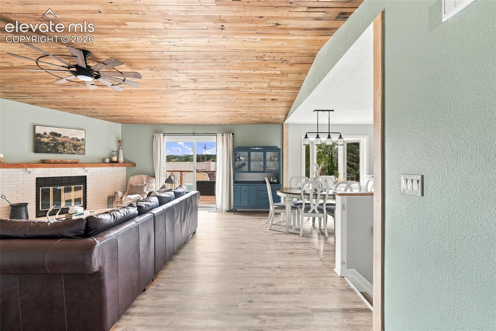 Vaulted wood-finish ceiling with a ceiling fan, white brick fireplace, wood-finish flooring, and sliding glass door