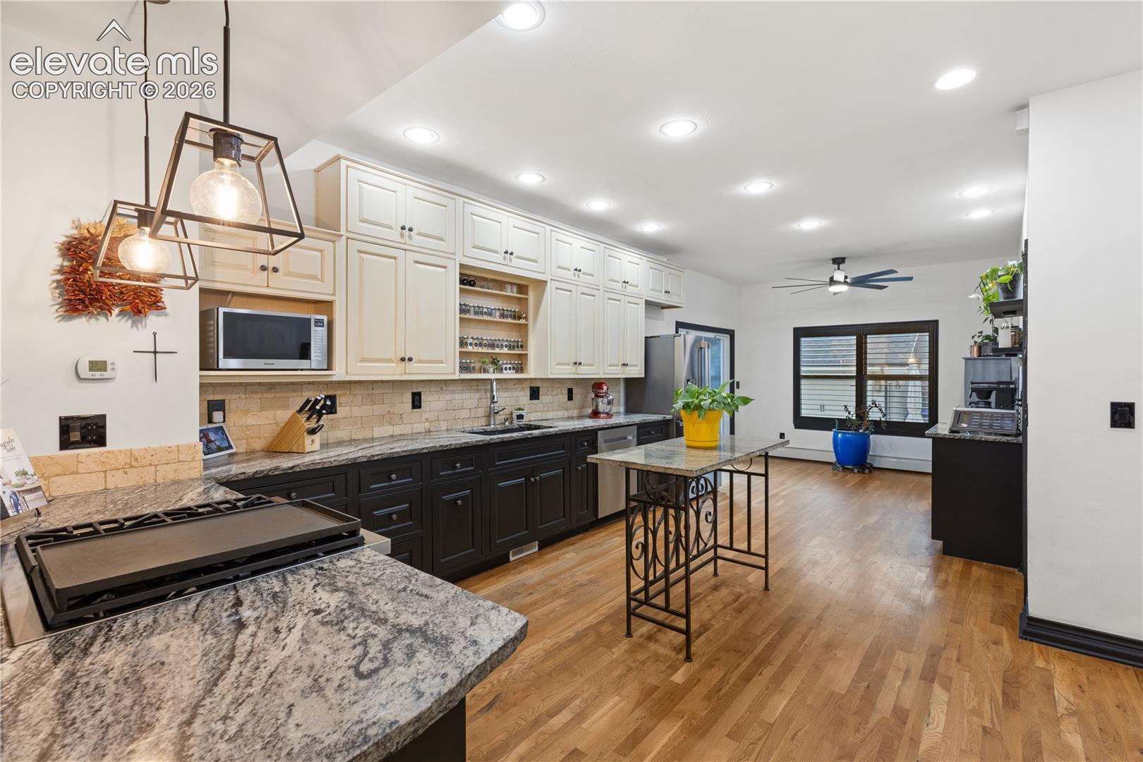 Spacious kitchen featuring two-tone cabinetry with black base cabinets and cream upper cabinets, a light-colored subway tile backsplash, and dark granite countertops