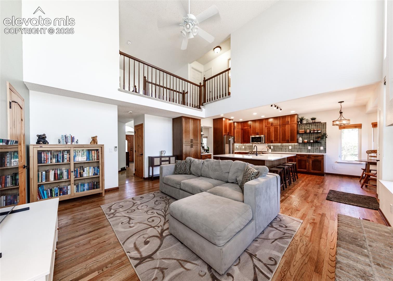 Vaulted ceilings, wood-finish flooring, open-concept living area, kitchen island with seating, and a second-story interior balcony
