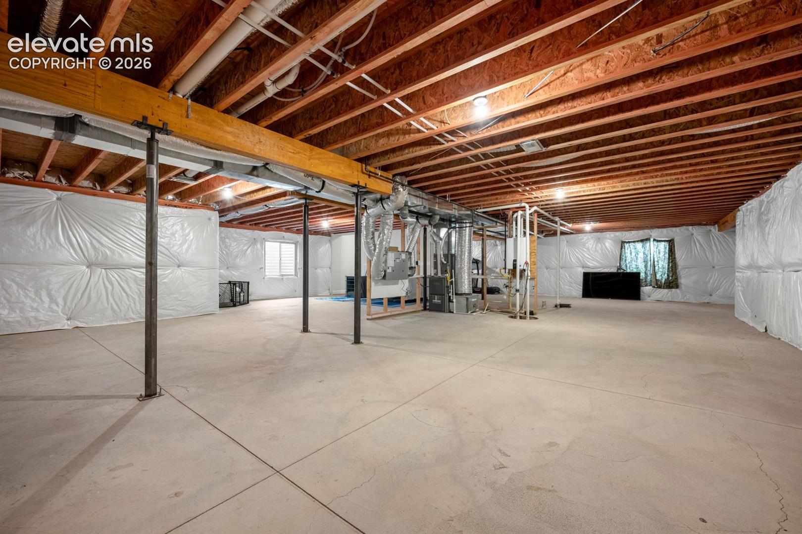 Unfinished lower level featuring an open floor plan, exposed wood ceiling joists, concrete flooring, and moisture-resistant wall vapor barriers supported by steel structural columns