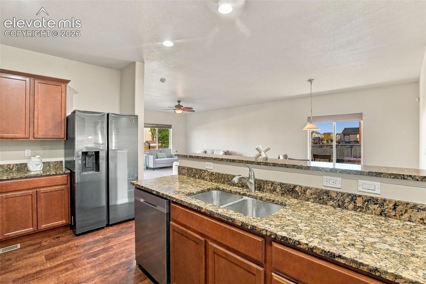 Kitchen featuring wood cabinetry, stone-finish countertops, stainless steel appliances, double-basin undermount sink, and wood-finish flooring