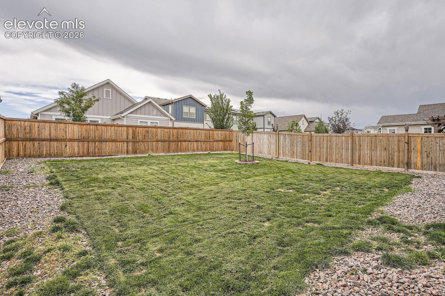 Fenced backyard featuring a manicured lawn, gravel perimeter, and mature tree