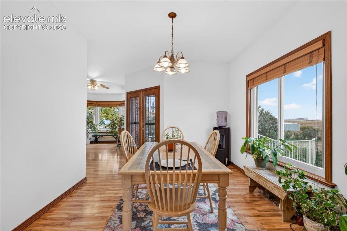 Dining area featuring wood-finish flooring, a multi-light chandelier, expansive windows with wood trim, and a double-door entry with decorative security grilles