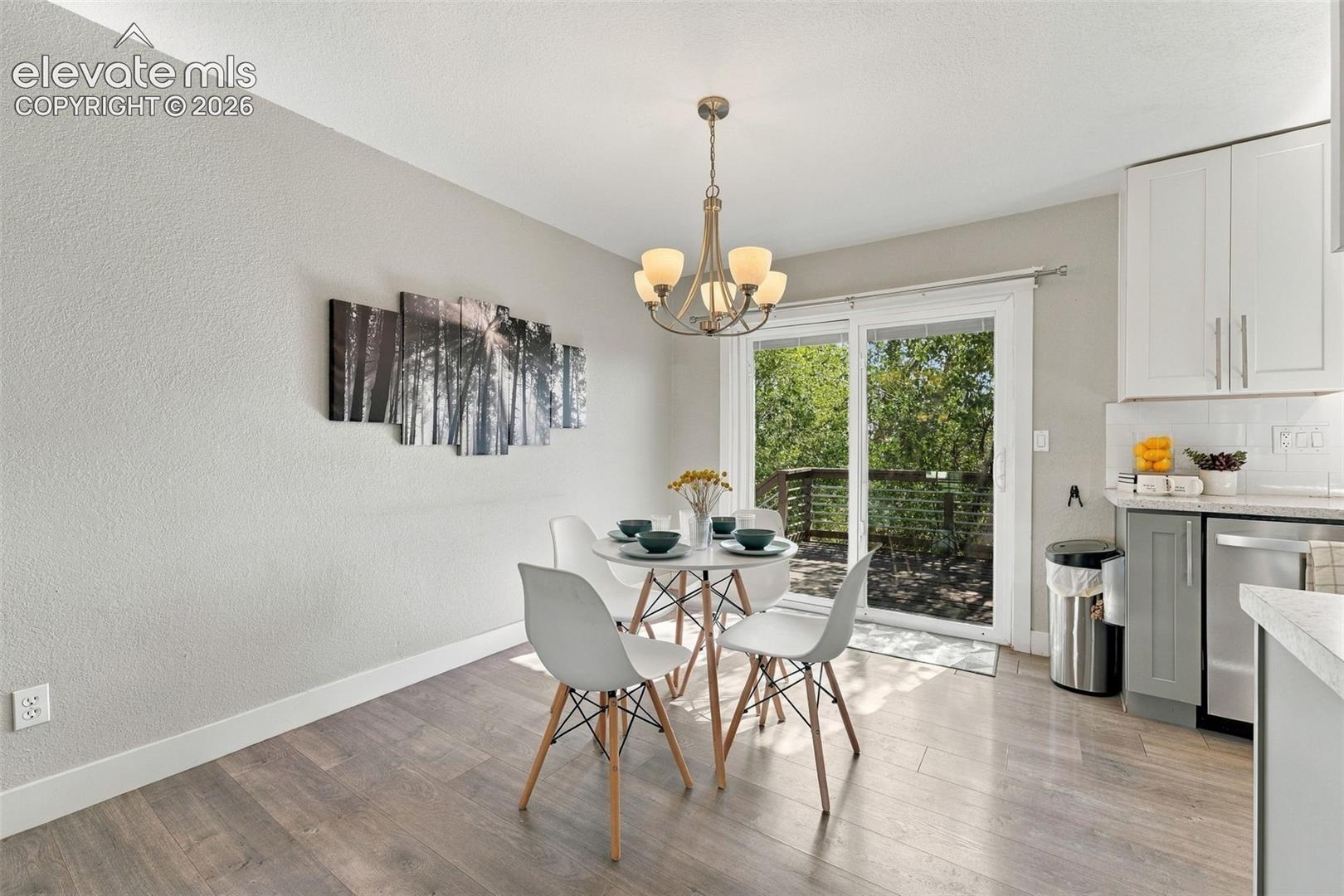 Wood-finish flooring with white baseboards, sliding glass door, overhead chandelier, white upper cabinetry, and stainless steel appliances