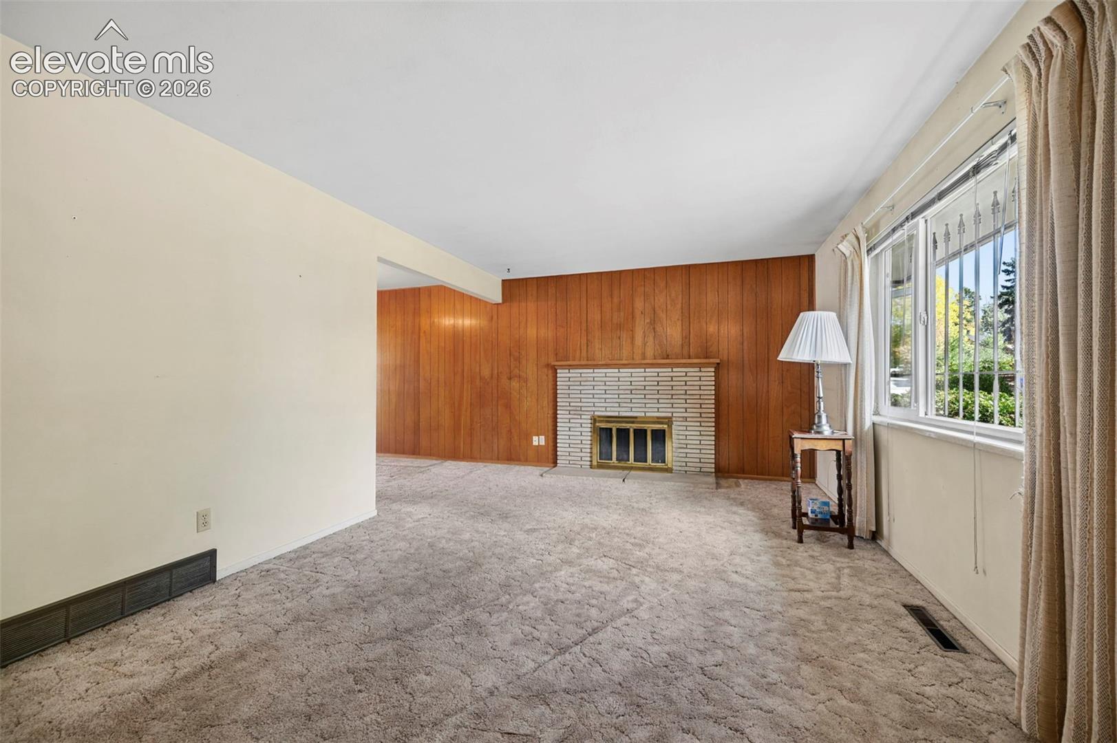 Large, bright Living Room with wood-paneled accent wall, masonry fireplace with metal screen, wall-to-wall carpeting, and large window  