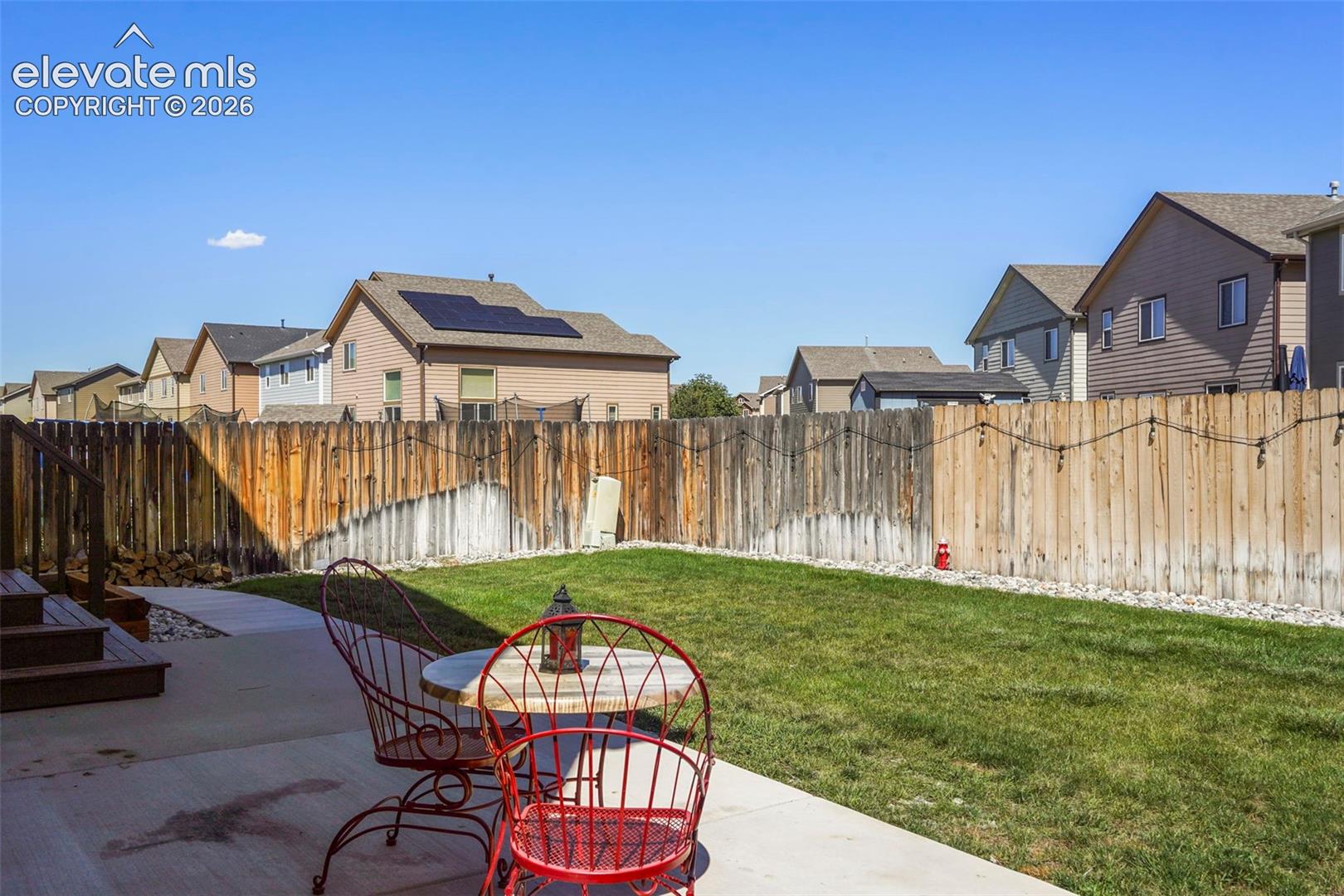 Expansive grassy lawn with a concrete patio, wood privacy fencing, and wood deck with stairs