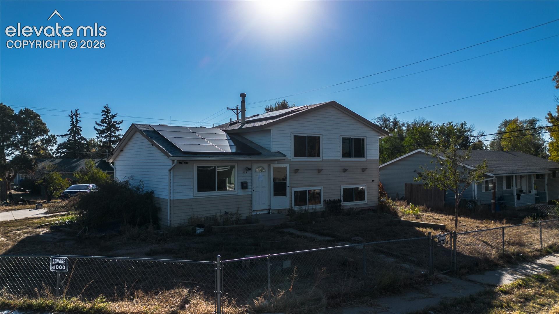 Split-level residence featuring dual-tone siding, roof-mounted solar panels, and a chain-link fenced perimeter