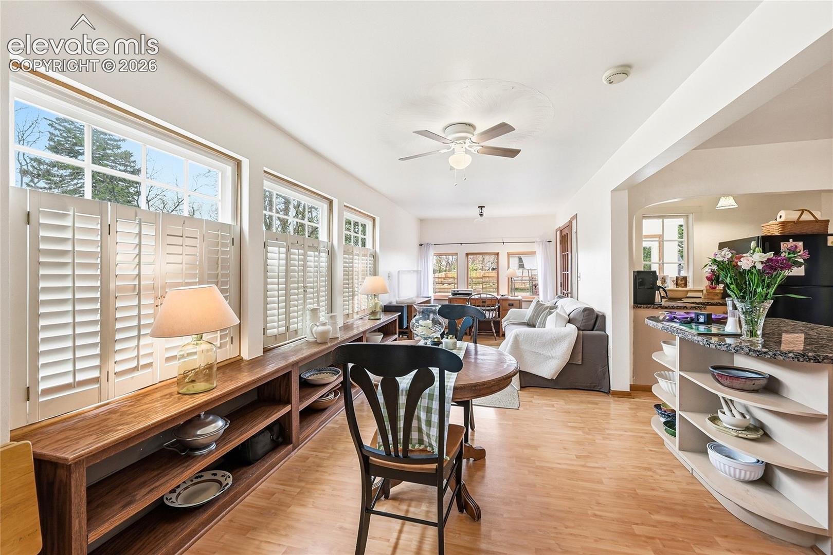 Sun-drenched interior featuring wood-finish flooring, custom built-in low-profile cabinetry, plantation shutters, and a kitchen peninsula with integrated curved display shelving
