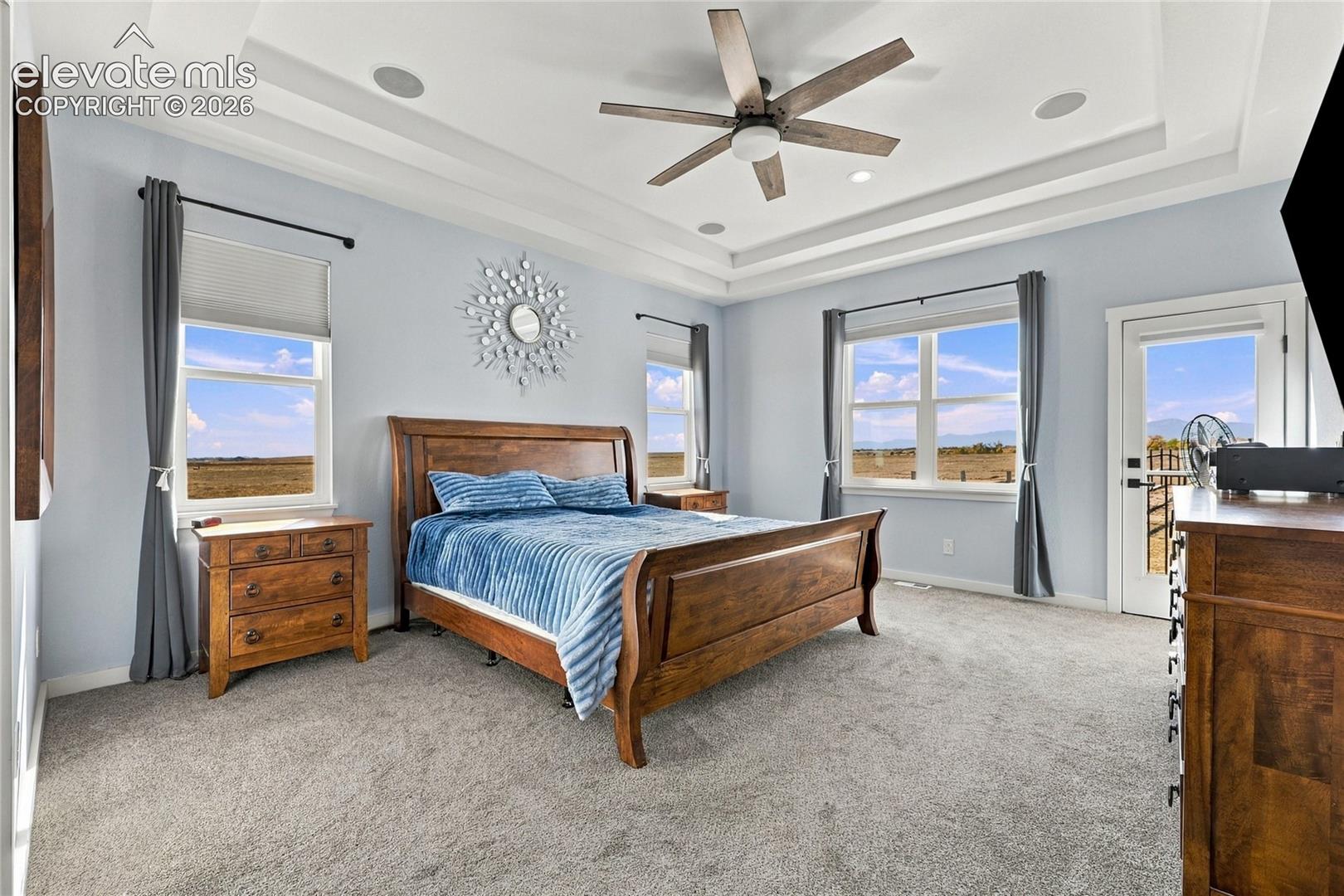 Bedroom featuring a tiered tray ceiling, neutral wall-to-wall carpeting, recessed lighting, and a ceiling fan