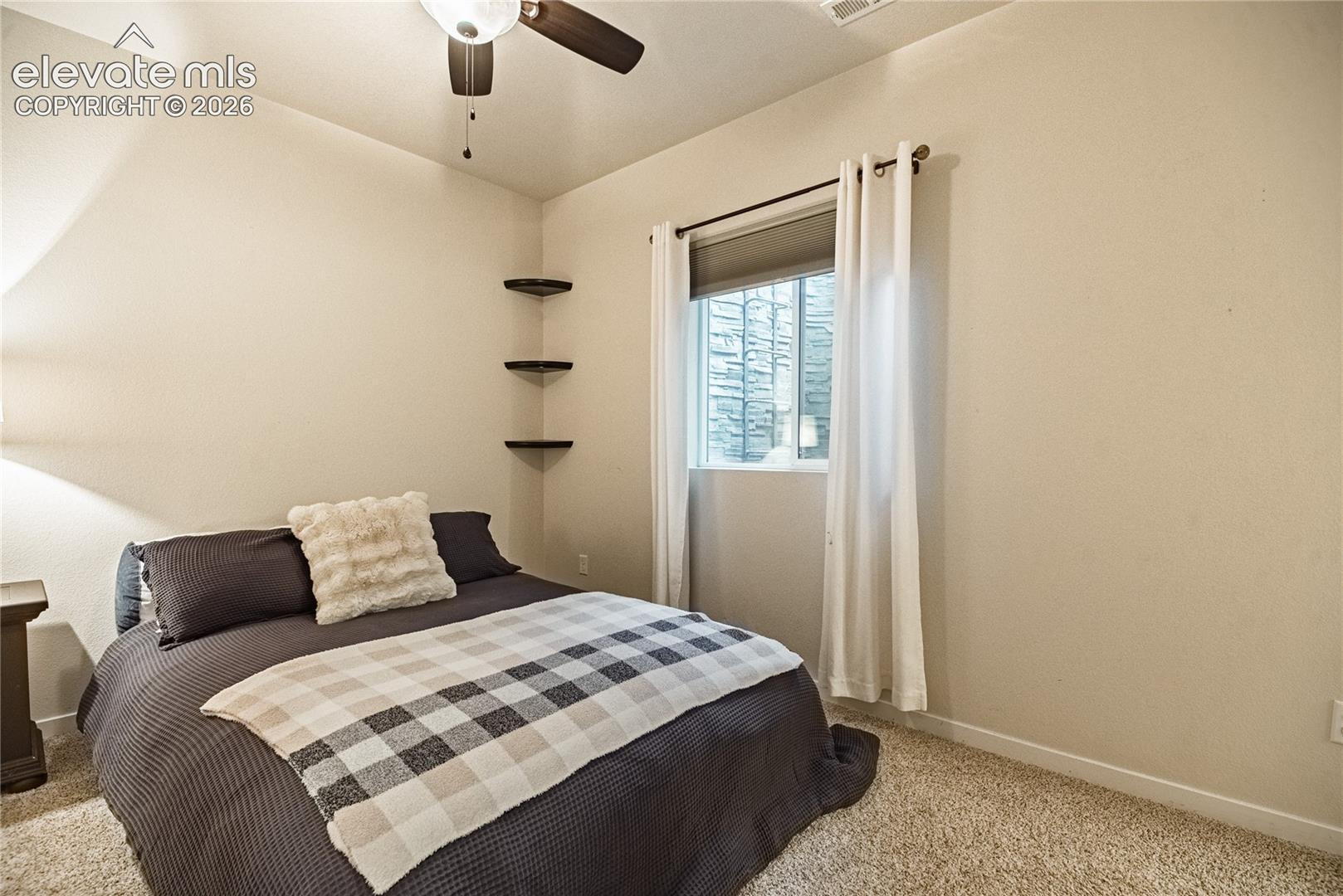 Neutral-toned room featuring wall-to-wall carpeting, three built-in corner shelves, and a ceiling-mounted fan with light fixture