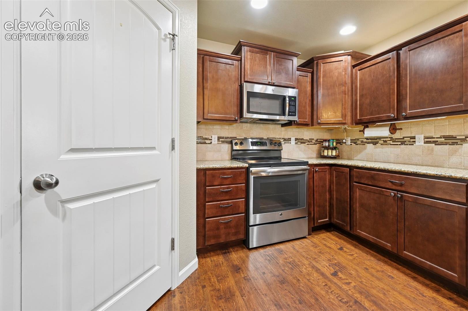 Kitchen featuring vinyl flooring, dark wood cabinetry, light-toned countertops, a tile backsplash with decorative accents, pantry and stainless steel appliances including a range and microwave