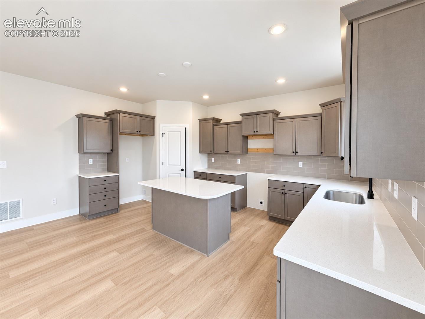 Kitchen featuring neutral-toned cabinetry, solid surface countertops, a central island, subway tile backsplash, and wood-finish flooring